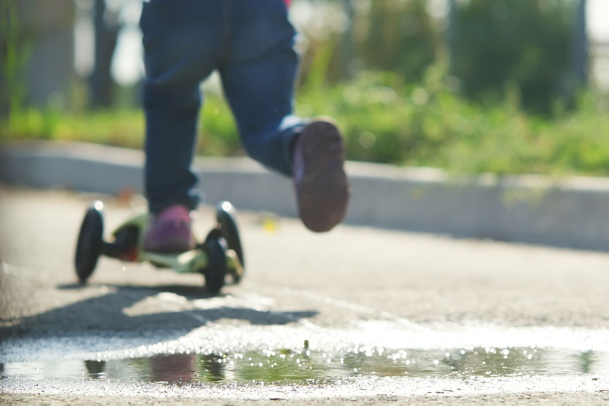 Kind fährt mit Trottinett auf der Strasse.