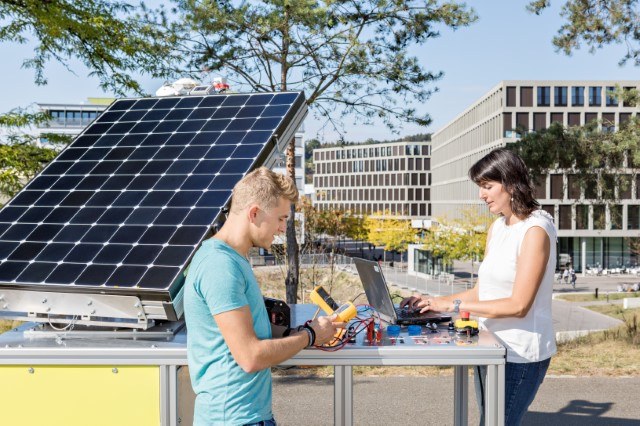 Zwei Lernende mit elektronischen Messgeräten neben einer Fotovolatiktafel 