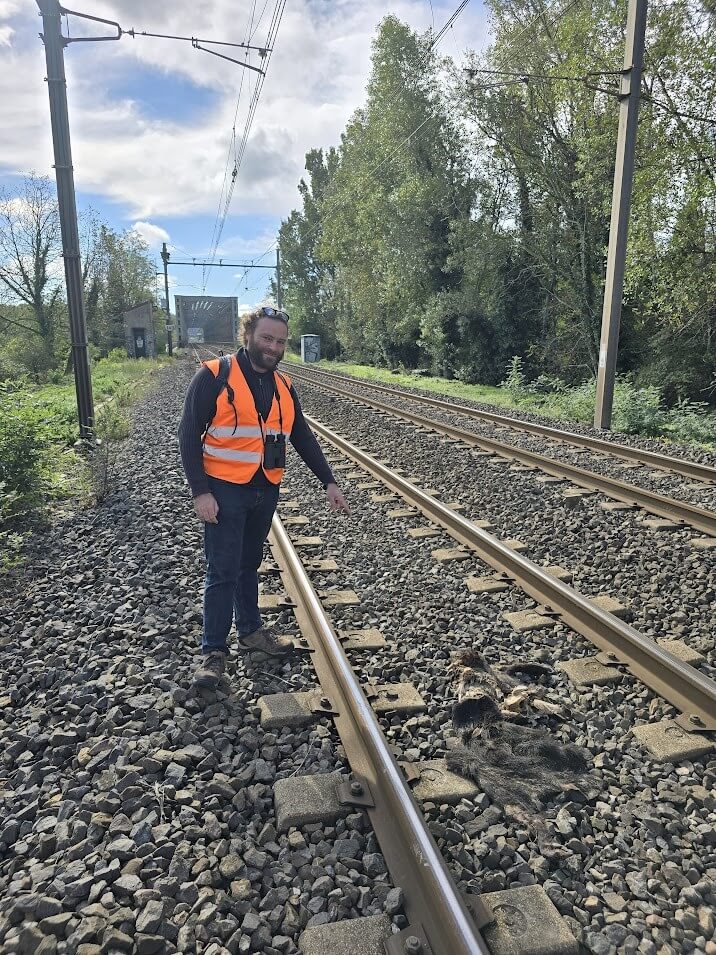 Adrian Meyer steht auf dem Bahngleis und hat eine orange Warnweste an. Er zeigt mit dem Finger auf schwarze Haufen auf den Gleisen.
